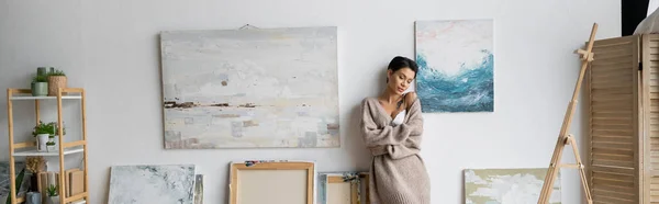 Sexy short haired artist in bra and sweater standing in workshop, banner - foto de stock