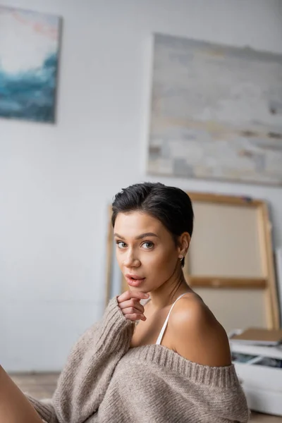 Portrait of sexy artist in sweater looking at camera in workshop — Stockfoto