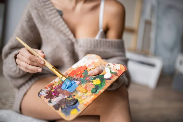 Cropped view of burred artist holding paintbrush and palette in workshop — Foto stock