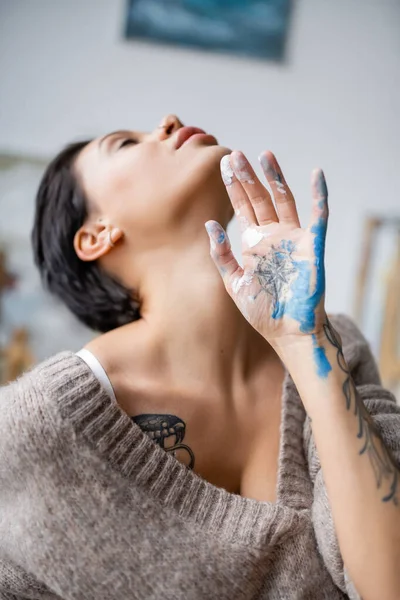 Blurred tattooed artist with paint on hand posing in workshop — Stock Photo