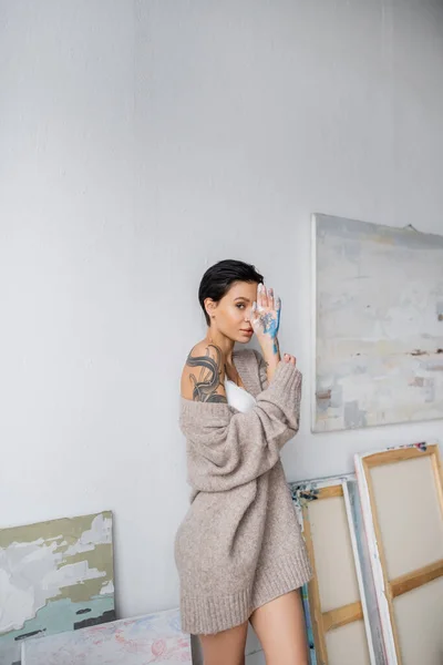 Sensual artist covering face with hand in paint in workshop — Stock Photo