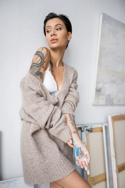 Sexy tattooed artist with paint on hand posing in workshop - foto de stock