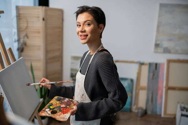 Smiling artist looking at camera while painting on canvas in studio — Foto stock