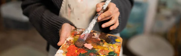 Cropped view of woman in apron holding palette and paintbrush, banner — Stock Photo