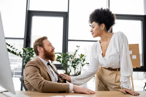 Side view of sensual african american woman pulling tie while seducing bearded coworker in office — Stock Photo