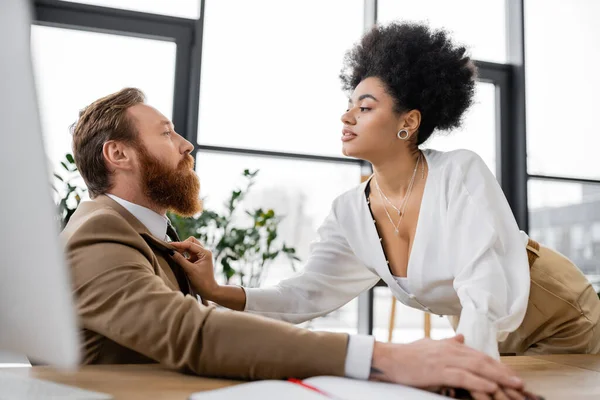 Curly african american woman adjusting jacket of bearded man in office — Stock Photo