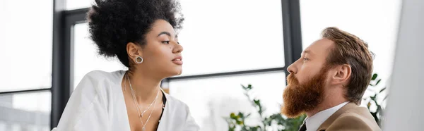 Curly african american woman looking at bearded man in office, banner — Stock Photo