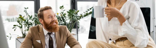 African american woman holding cup of coffee near happy businessman with beard, banner — Photo de stock