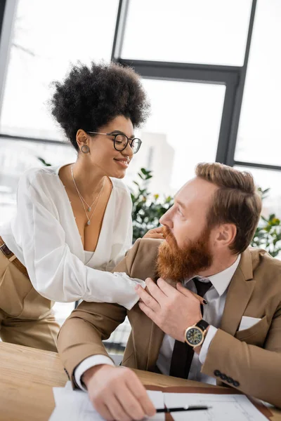 Smiling african american businesswoman seducing and touching coworker in office — Stock Photo