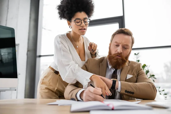 Curly african american businesswoman pointing at documents and seducing tattooed coworker in office — Stock Photo