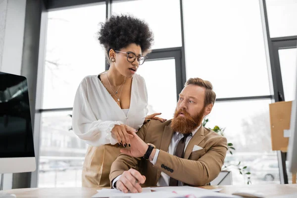 Curly african american woman trying to seduce displeased businessman working with documents — Stock Photo