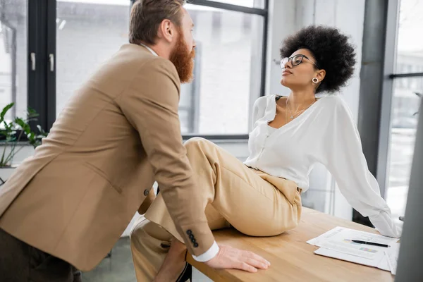 African american woman sitting on office desk and seducing bearded man — Stock Photo