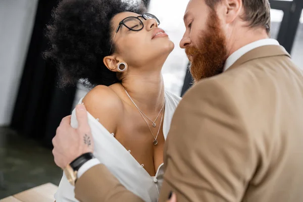 Tattooed man undressing seductive african american woman in office — Stock Photo