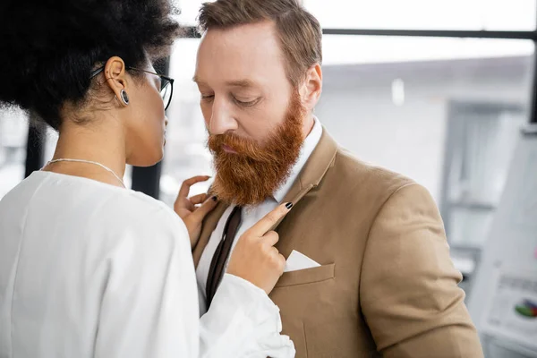 Seductive african american woman adjusting blazer of bearded man in formal wear — Stock Photo