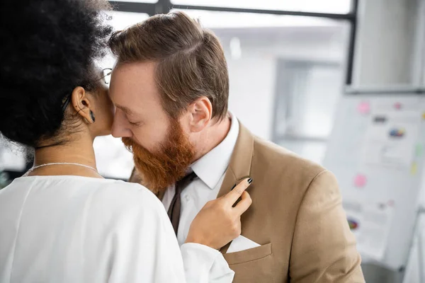 Seductive african american woman adjusting blazer of bearded businessman in formal wear — Stock Photo