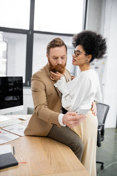 Curly african american woman seducing bearded businessman with smartphone — Stock Photo
