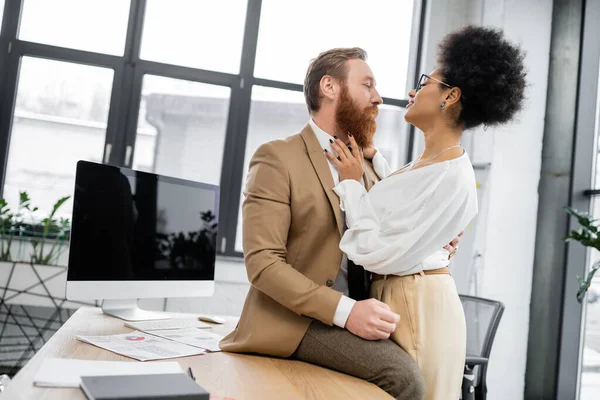 Curly african american woman seducing bearded businessman near computer monitor in office — Stock Photo