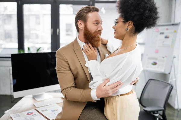 Cheerful african american woman seducing bearded businessman near computer monitor in office — Stock Photo