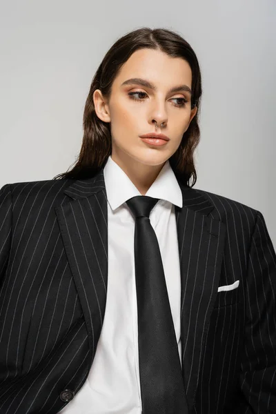 Brunette woman in white shirt and black striped jacket with tie isolated on grey - foto de stock