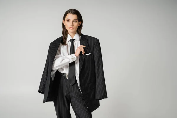 Brunette model in white shirt and black trousers with blazer looking at camera isolated on grey — Fotografia de Stock