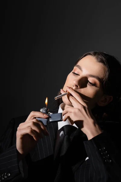 Молода і елегантна жінка в формальному носінні освітлення сигарети ізольовані на чорному — стокове фото