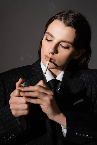 Portrait of young model in formal wear lighting cigarette isolated on dark grey - foto de stock