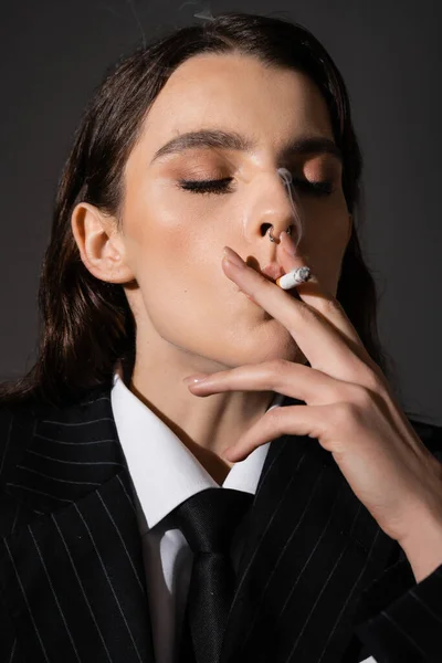 Портрет молодої жінки в стильному формальному одязі куріння з закритими очима ізольовано на темно-сірому — стокове фото