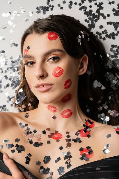 Top view of sexy woman with bare shoulders and red lipstick marks lying near silver shiny confetti on grey — Fotografia de Stock