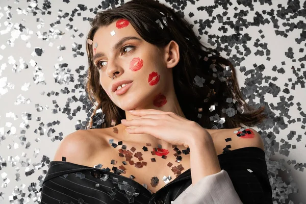 Top view of young brunette woman with red lip prints looking away near sparkling silver confetti on grey background — Foto stock