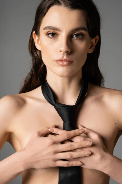 Front view of shirtless woman in black tie covering breast with hands and looking at camera isolated on grey - foto de stock