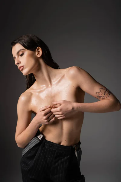 Sexy shirtless woman covering bust with hands while posing in black striped trousers on grey background — Stock Photo