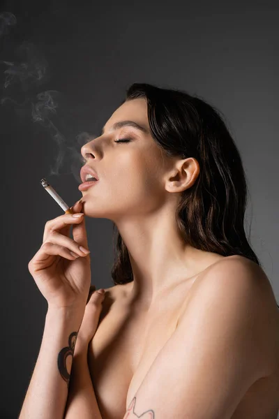 Sensual shirtless woman covering breast and smoking isolated on grey — Stock Photo