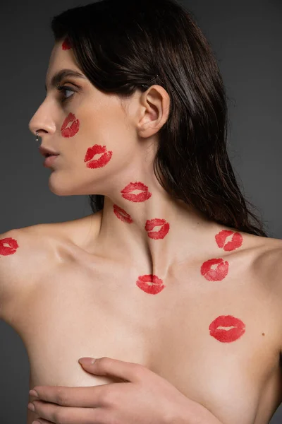 Young shirtless woman with red lipstick marks covering breast with hand while looking away isolated on grey — Stock Photo