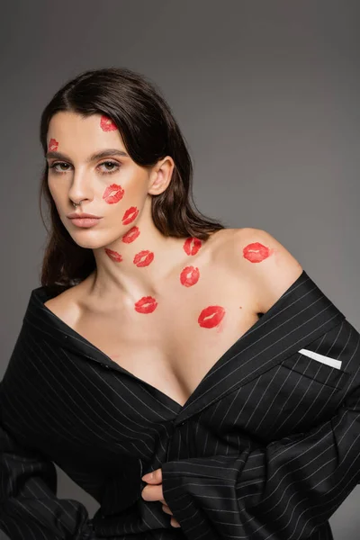 Чуттєва брюнетка жінка в оверсайз Блейзер позує з червоним поцілунком на тілі і обличчі ізольована на сірому — стокове фото