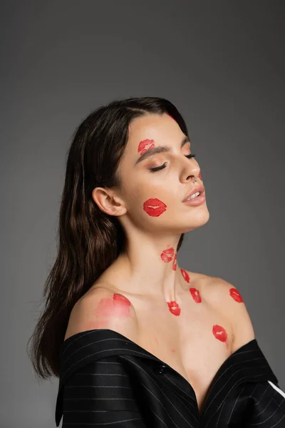 Portrait of young sensual woman with red lipstick marks on body and bare shoulders posing with closed eyes isolated on grey — Stock Photo