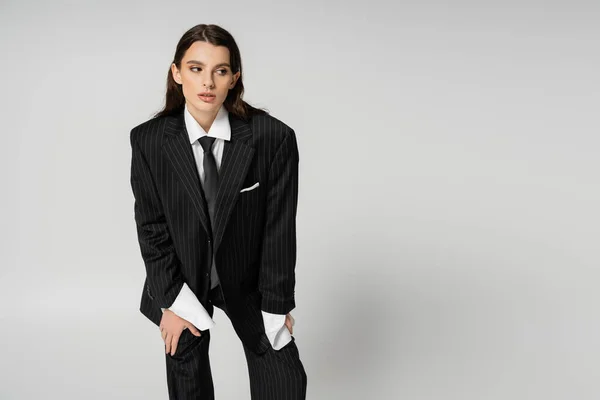 Young brunette woman in black striped suit and tie looking away isolated on grey — Photo de stock