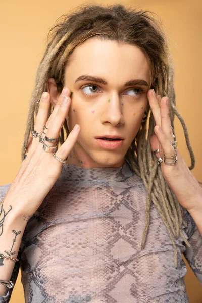 Portrait of queer person with dreadlocks touching face on yellow background — Stock Photo