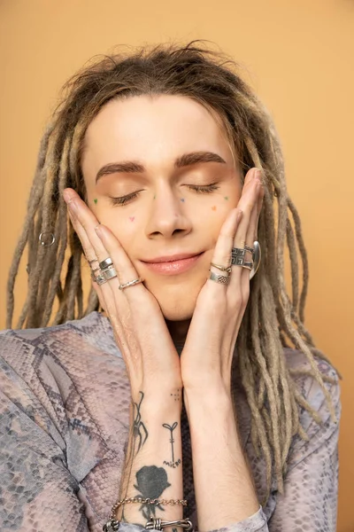 Portrait of pleased tattooed queer person touching face isolated on yellow - foto de stock