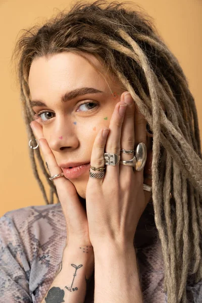 Portrait of tattooed nonbinary person touching face isolated on yellow - foto de stock