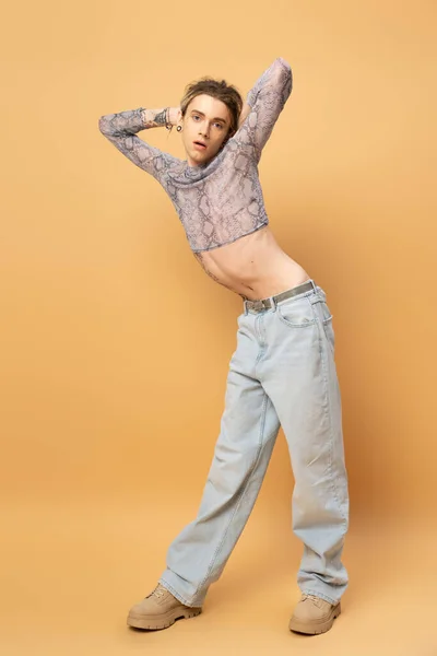 Full length of stylish queer person in top and jeans standing on yellow background - foto de stock