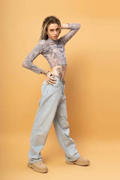 Full length of tattooed nonbinary person looking at camera on yellow background — стоковое фото