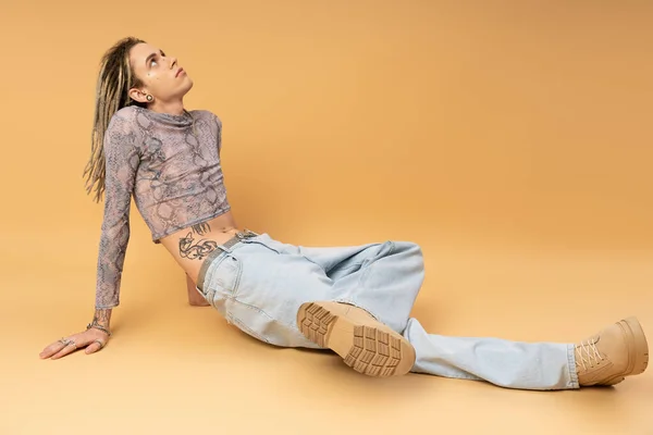 Young queer person in crop top and jeans sitting on yellow background — Photo de stock