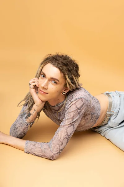 Smiling tattooed queer person in top looking at camera on yellow background - foto de stock