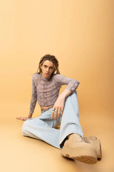 Stylish queer person in jeans and crop top sitting on yellow background — Stockfoto