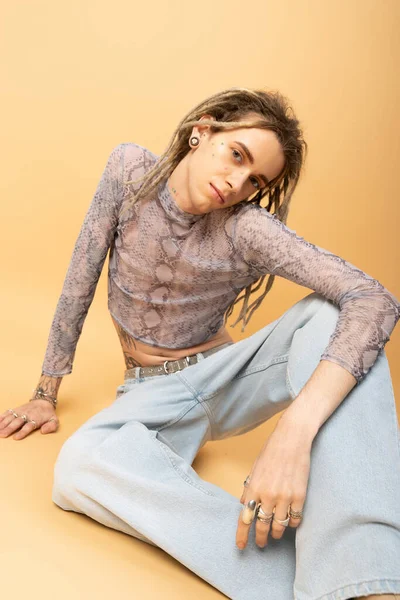 Tattooed nonbinary person with dreadlocks sitting on yellow background - foto de stock