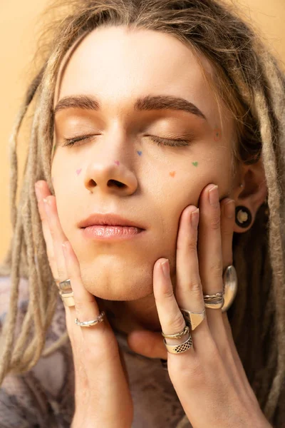 Portrait of tattooed queer person touching face isolated on yellow - foto de stock