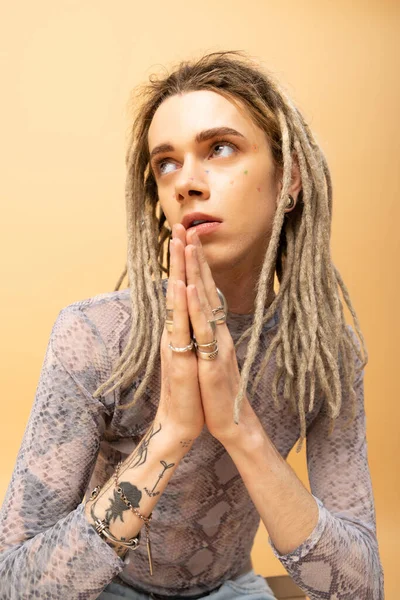 Tattooed queer person doing praying hands gesture on yellow background — Stock Photo
