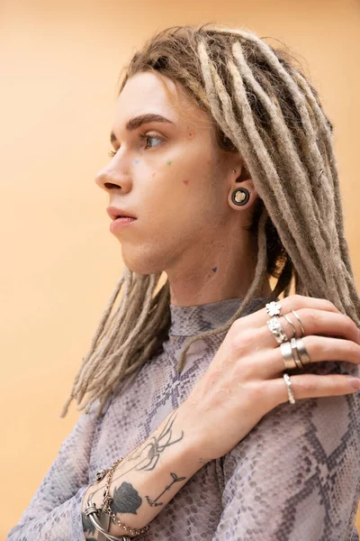 Portrait of tattooed queer person with dreadlocks touching shoulder isolated on yellow — стоковое фото