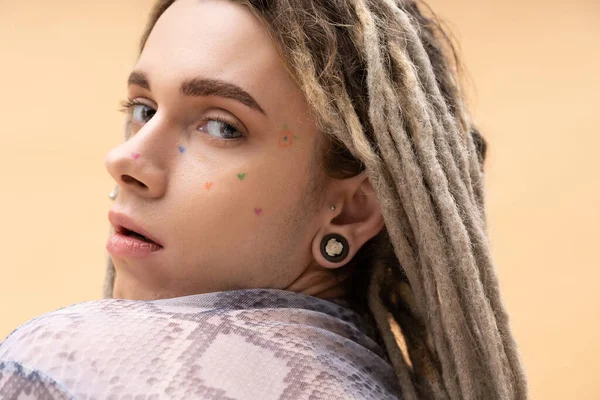 Portrait of young nonbinary person with tattoo and dreadlocks posing isolated on yellow - foto de stock