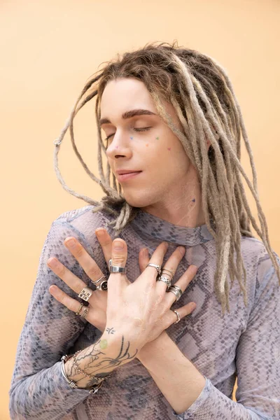 Pleased queer person with dreadlocks touching chest isolated on yellow - foto de stock
